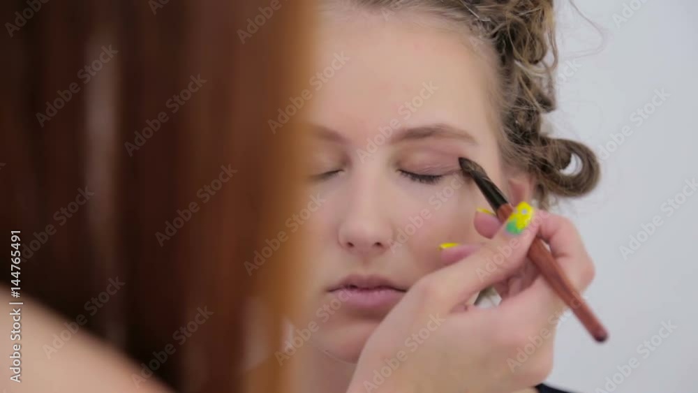 Professional make-up artist applies eye shadow to eyelid of model in white room. Beauty, makeup and fashion concept Professional make-up artist applies eye shadow to eyelid of model in white room. Beauty, makeup and fashion concept