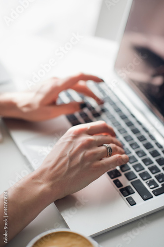 Close-up picture of woman's hands typing a message on her laptop during lunch.