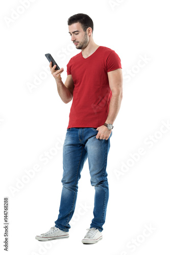 Relaxed young casual man reading text message on mobile phone. Full body length portrait isolated over white studio background.