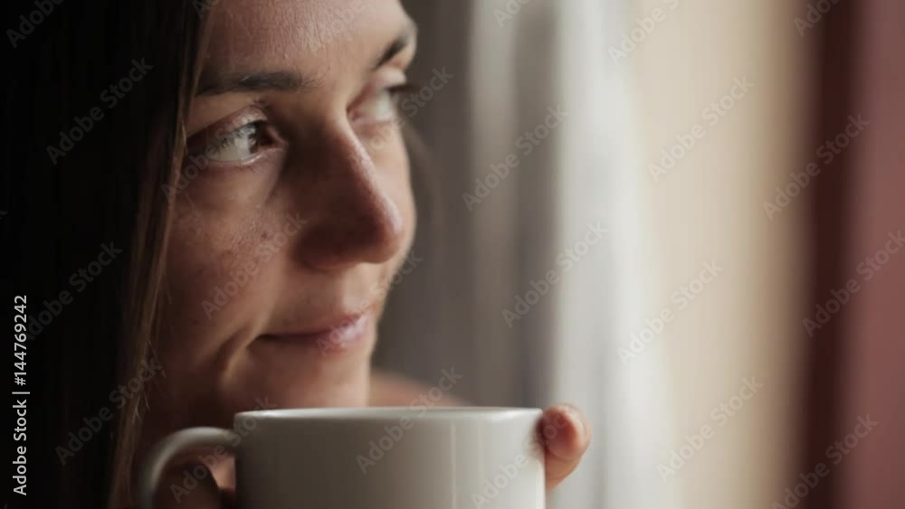 Young attractive woman sitting near the window and drinking tea Young attractive woman sitting near the window and drinking tea