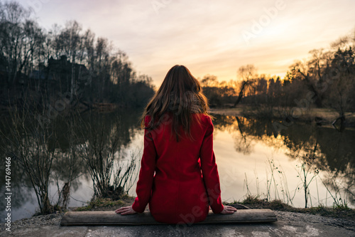 Young woman sitting and looking at the river at sunset