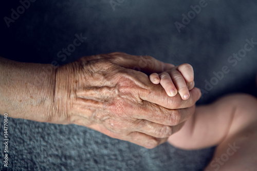 great-grandmother holds the hands of his beloved grandson by the window