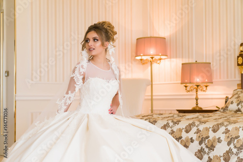 Portrait of beautiful young bride. A girl is posing in a hotel room. A lady Is worth with by the window. bride waiting in hotel.