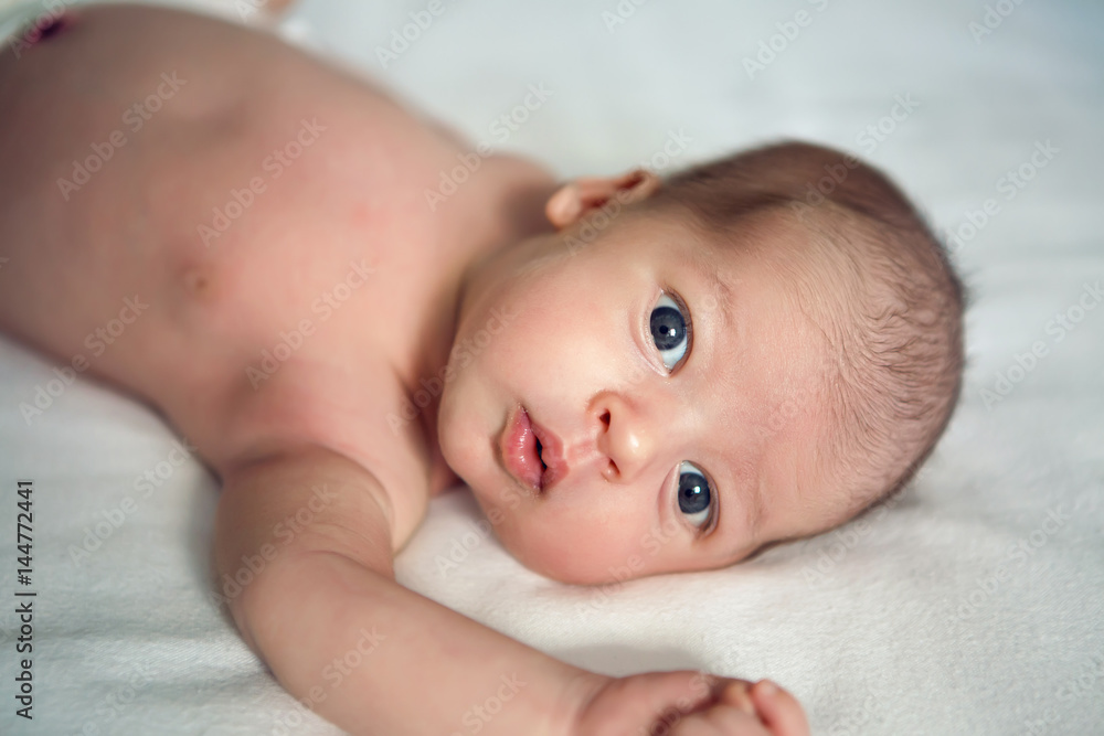 newborn baby looking at camera on bed on white background newborn baby looking at camera on bed on white background