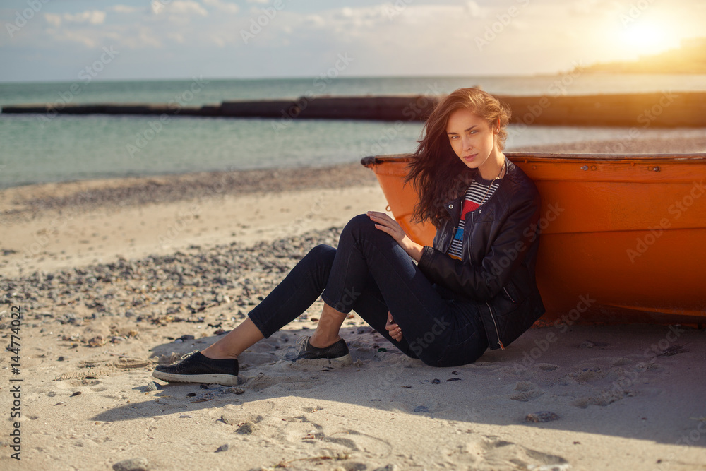 A girl sideways near a red boat on the beach by the sea