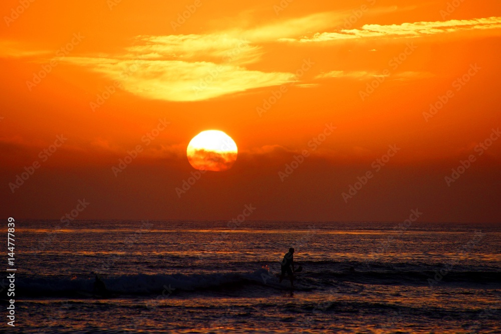 Orange sunset over the Pacific with paddle-boarders 