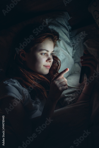 woman in the dark lies on the bed and looks into the phone