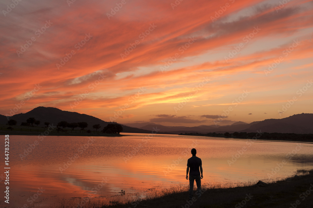 Naklejka premium Man on the lake shore contemplates an amazing sunset