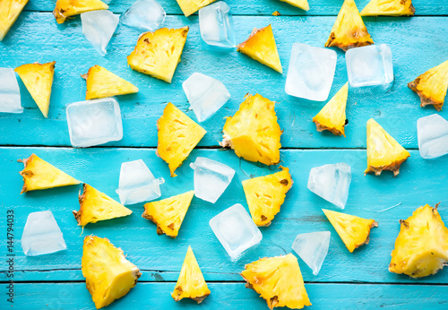 the summer pineapple is slice for eat with cold ice on blue wooden background.