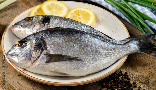 Fresh uncooked dorado fish with lemon and spices on a wooden board