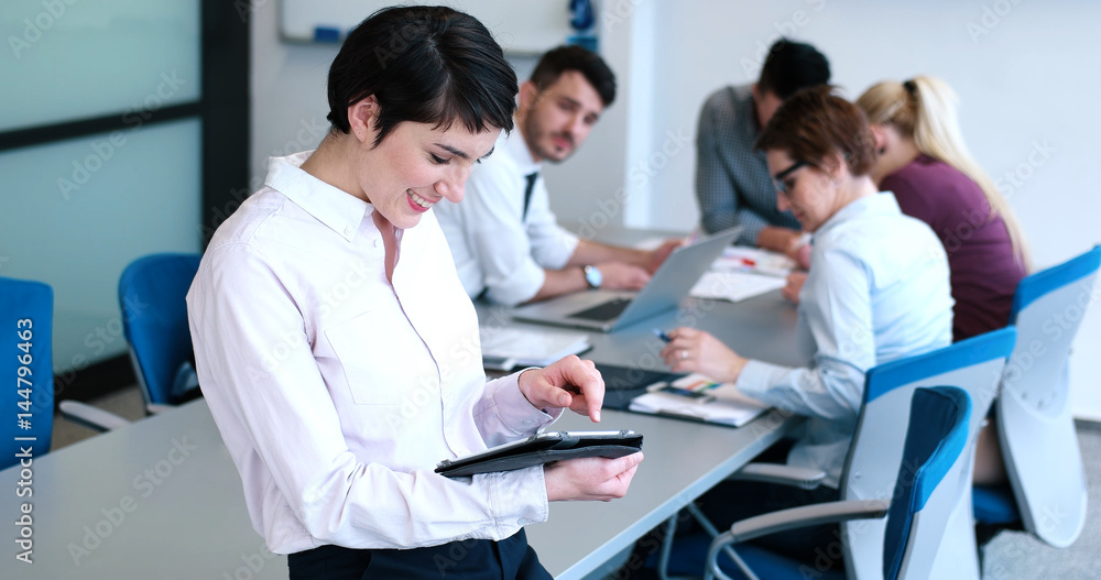 Portrait of smiling casual businesswoman using tablet with coworkers standing in background Portrait of smiling casual businesswoman using tablet with coworkers standing in background