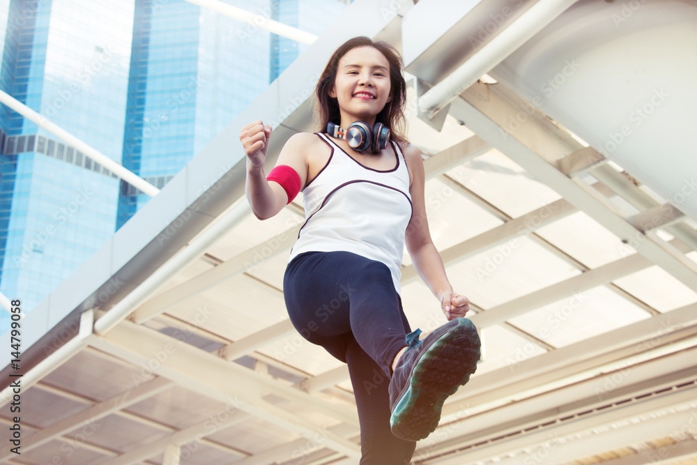 Woman wears sport wears is exercising warm up her body before go jogging in the city. She got big headphone to listen the music. She enjoy her life. Woman wears sport wears is exercising warm up her body before go jogging in the city. She got big headphone to listen the music. She enjoy her life.