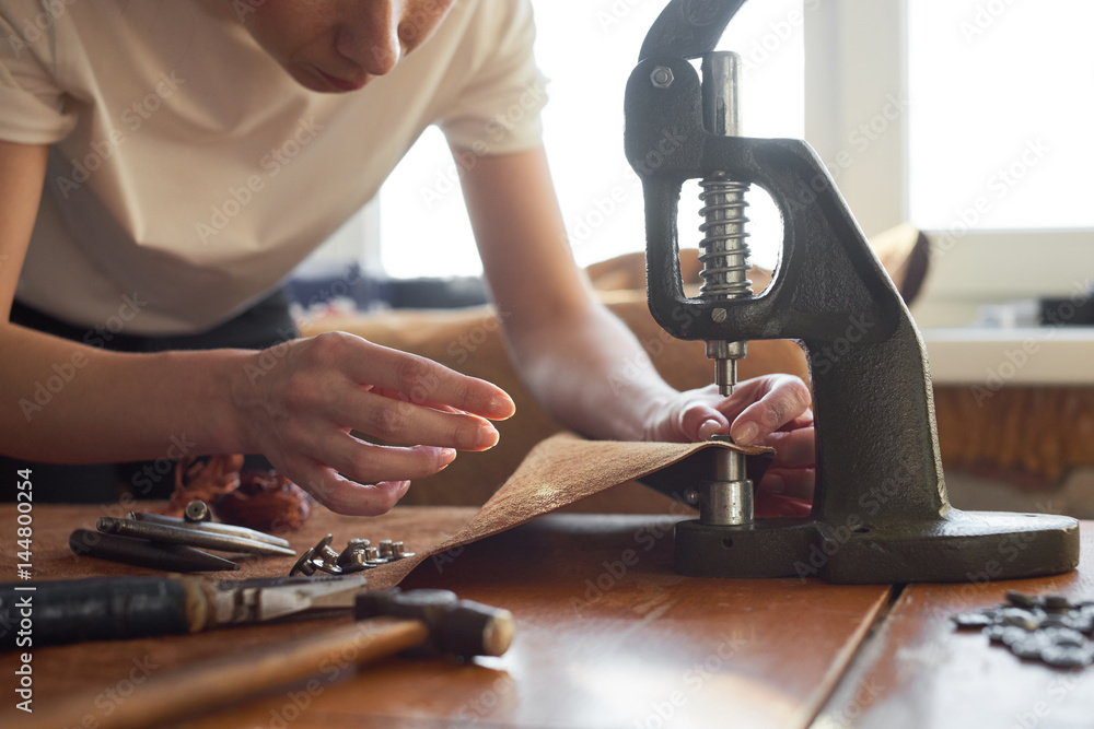 Female artisan using manual vintage machine tool for pinching buttons on leather material