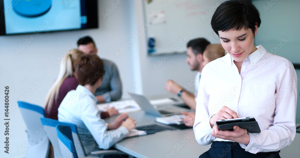 Portrait of smiling casual businesswoman using tablet with coworkers standing in background Portrait of smiling casual businesswoman using tablet with coworkers standing in background