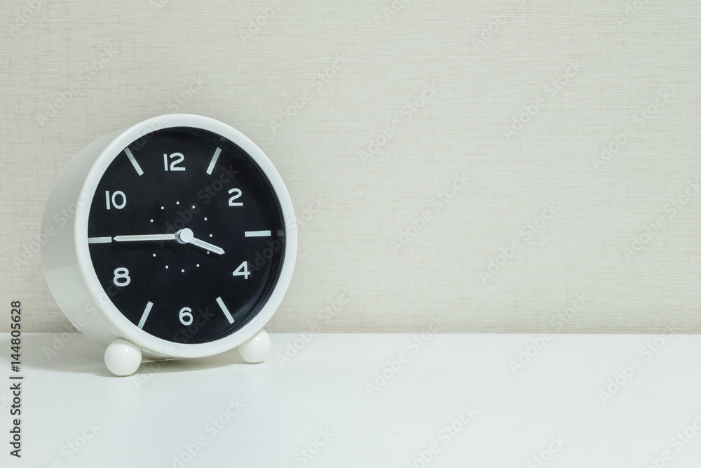 Closeup black and white alarm clock for decorate in a quarter to four o'clock or 3:45 p.m. on white wood desk and cream wallpaper textured background with copy space