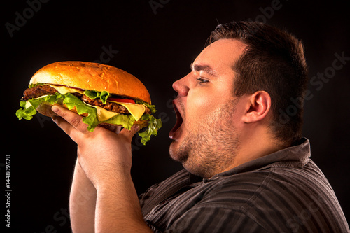 Diet failure of fat man eating fast food hamberger. Breakfast for overweight person who spoiled healthy food by eating huge hamburger. Junk meal leads to obesity. Person regularly overeats concept .