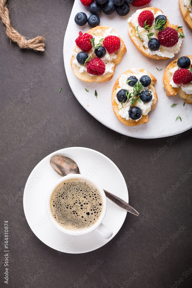 Cup of coffee with berry and goat cheese sandwiches on marble cutting board, top view, copy space. Cup of coffee with berry and goat cheese sandwiches on marble cutting board, top view, copy space.