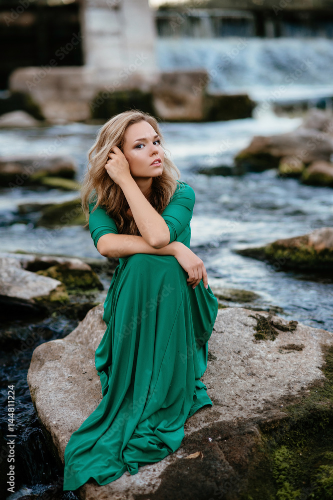 Beautiful girl posing on rocks near the water. Model in a green dress in nature. Beautiful girl posing on rocks near the water. Model in a green dress in nature.