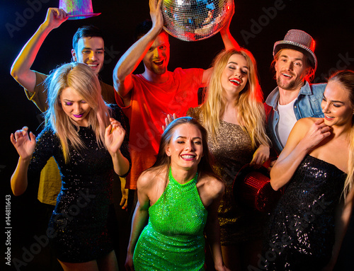 Dance party with group people dancing . Women and men have fun in night club. Happy girl in green evening dress on foreground and disco ball on background.