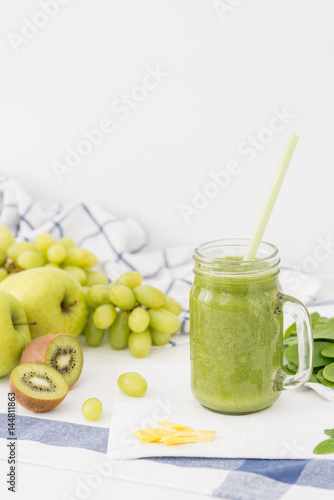 Green smoothie in glass jar made of apples, celery, grapes, spinach and kiwi on white cloth background. Healthy drink concept