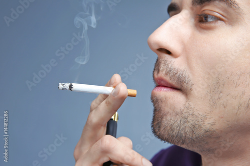 Young man smoking cigarette on color background