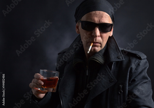 Rocker with glass of whiskey and cigarette on black background.