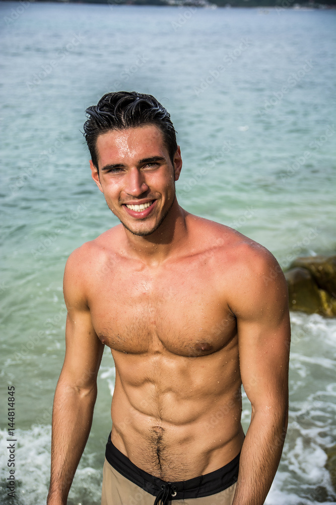 Attractive young man in the sea getting out of water with wet hair, looking in camera wiht a smile Attractive young man in the sea getting out of water with wet hair, looking in camera wiht a smile