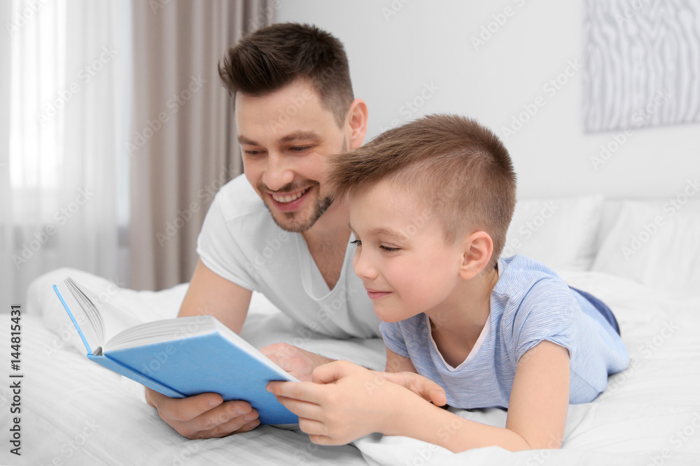 Dad and son reading interesting book while lying on bed at home Dad and son reading interesting book while lying on bed at home