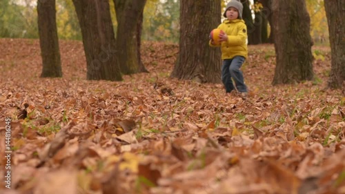 Happy playful three years old boy playing with ball in autumn park.