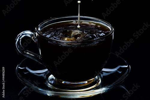 Drops of milk falling in a glass transparent cup with black coffee on a black background, studio light