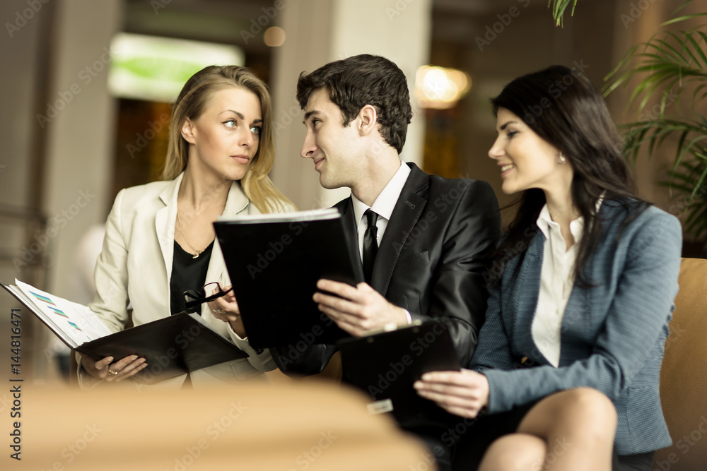 Business team discussing working papers sitting on the couch in the lobby of a modern office Business team discussing working papers sitting on the couch in the lobby of a modern office