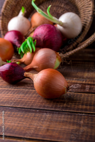 Different onions in basket on wooden background. Rustic style. Red, white and golden.