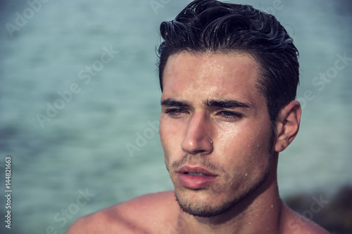 Attractive young man in the sea getting out of water with wet hair, looking away to a side