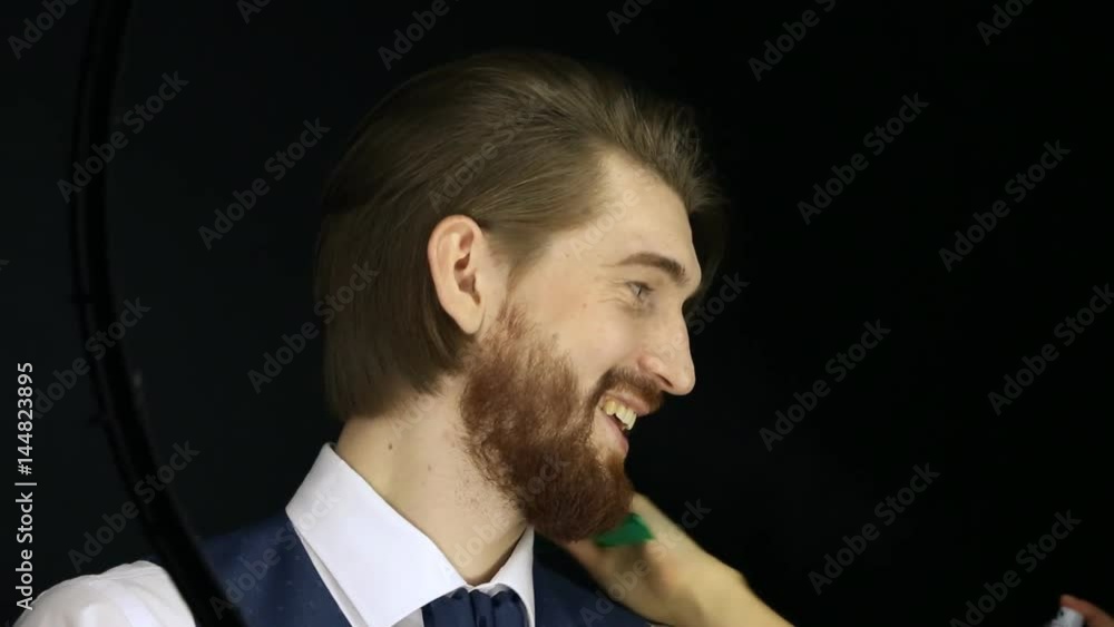 Elegant young bearded handsome man posing in fashionable suit. Young guy laughing and smiling during studio fashion shooting. Getting his hairdo done. Elegant young bearded handsome man posing in fashionable suit. Young guy laughing and smiling during studio fashion shooting. Getting his hairdo done.