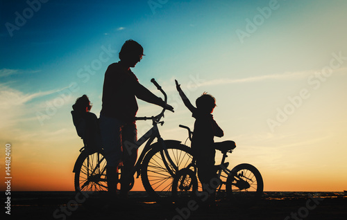 father with two kids on bikes at sunset beach