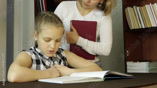 Upset little girl doing school tasks with mother, mom compels daughter to reads photo