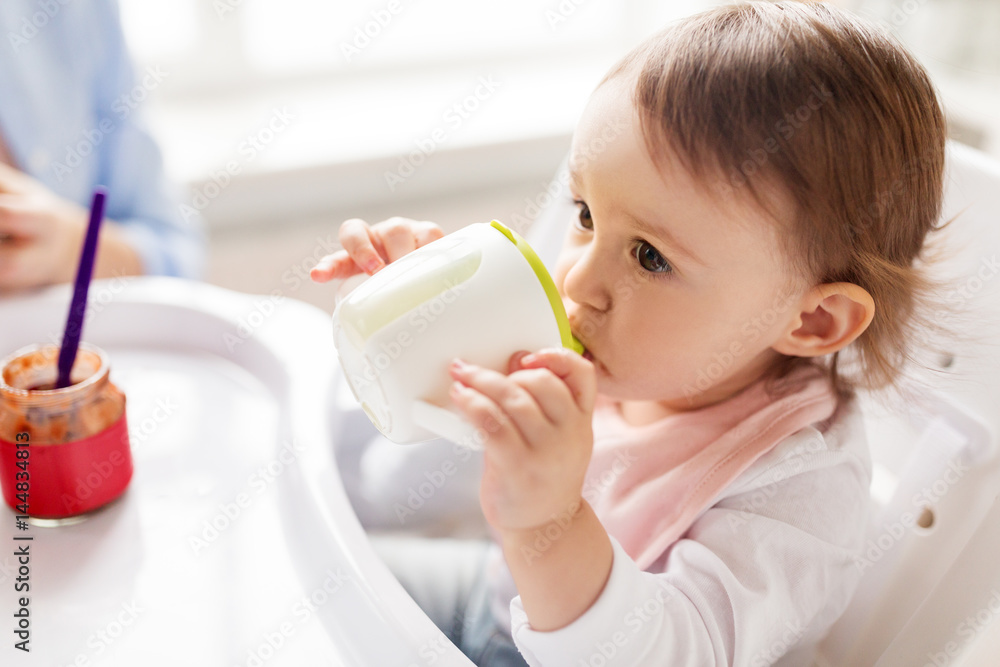 baby drinking from spout cup in highchair at home