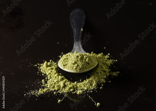 Green matcha tea powder on spoon, dark background.