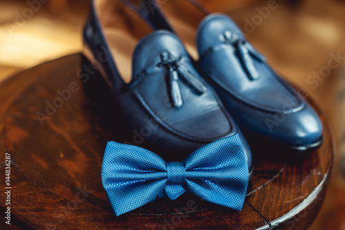 Blue shoes and bow tie on a wooden round stool. Accessory for formal dress. Symbol of elegance and fashion for men.