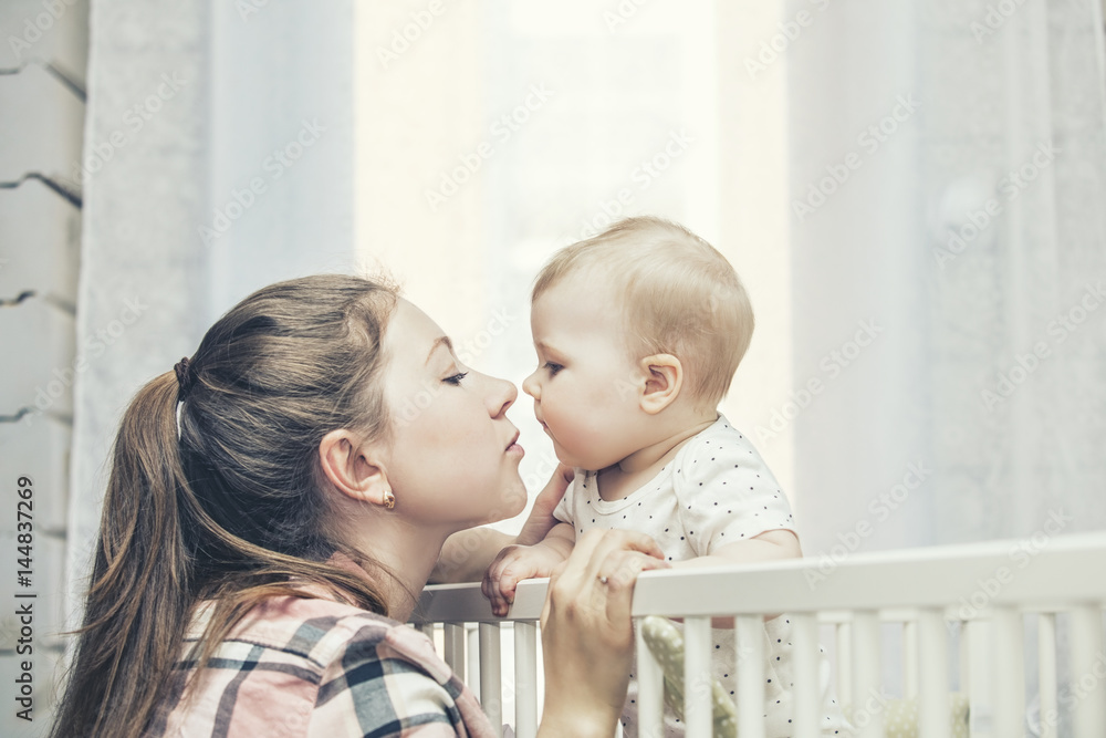 Mother and little baby is in the crib woke up in the morning and smiling Mother and little baby is in the crib woke up in the morning and smiling