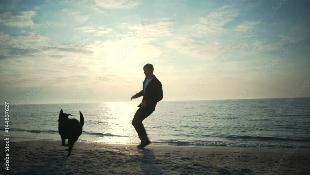 Young male run with his black dog at the sea slow motion Young male run with his black dog at the sea slow motion