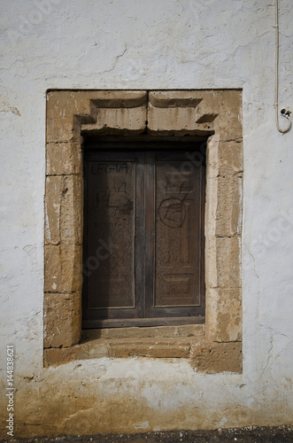 Ein altes Fenster mit geschlossenen Holzl  den in einem Fensterrahmen aus Natursteinen.  