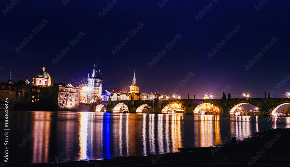 Charles bridge in Prague at night with lights reflected in water of Vltava