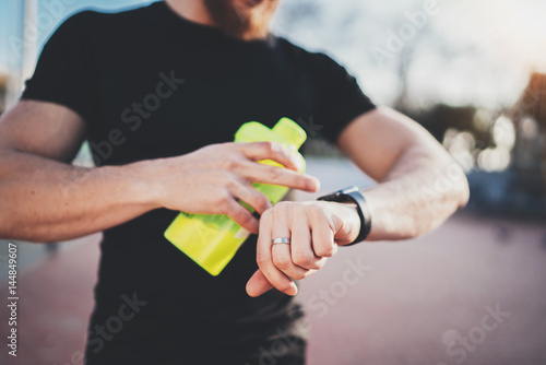 Muscular young athlete checking heart rate and burned calories on his smartphone application after good workout outdoor session on sunny park.Blurred background.