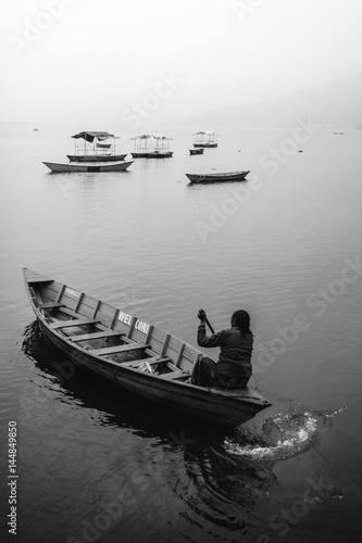 A woman alone in a canoe boat paddling on Fewa Lake, Pokhara on a misty morning in black and white. Pokhara, Nepal. photo