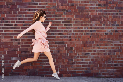 young woman jumping on city street with brick wall in background
