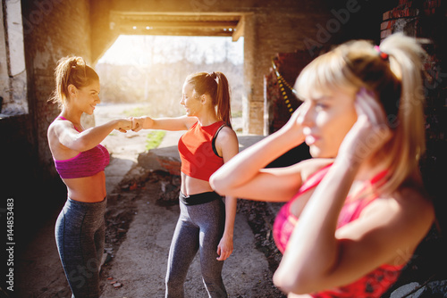 After workout girls clapping hands smiling positive energy. Group fitness people celebrating success at abandoned factory, hot summer day sunshine.