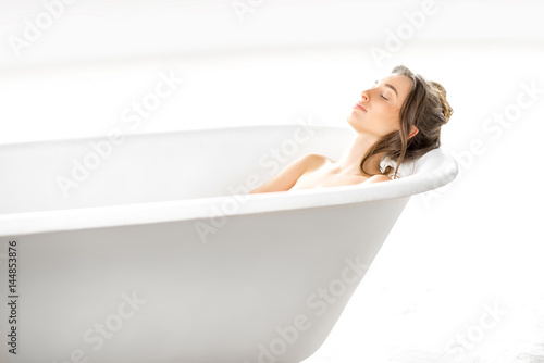 Beautiful young woman relaxing lying in the bathtube in the bright bathroom