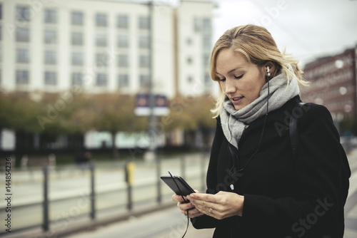 Mid adult businesswoman listening music through smart phone at tram station