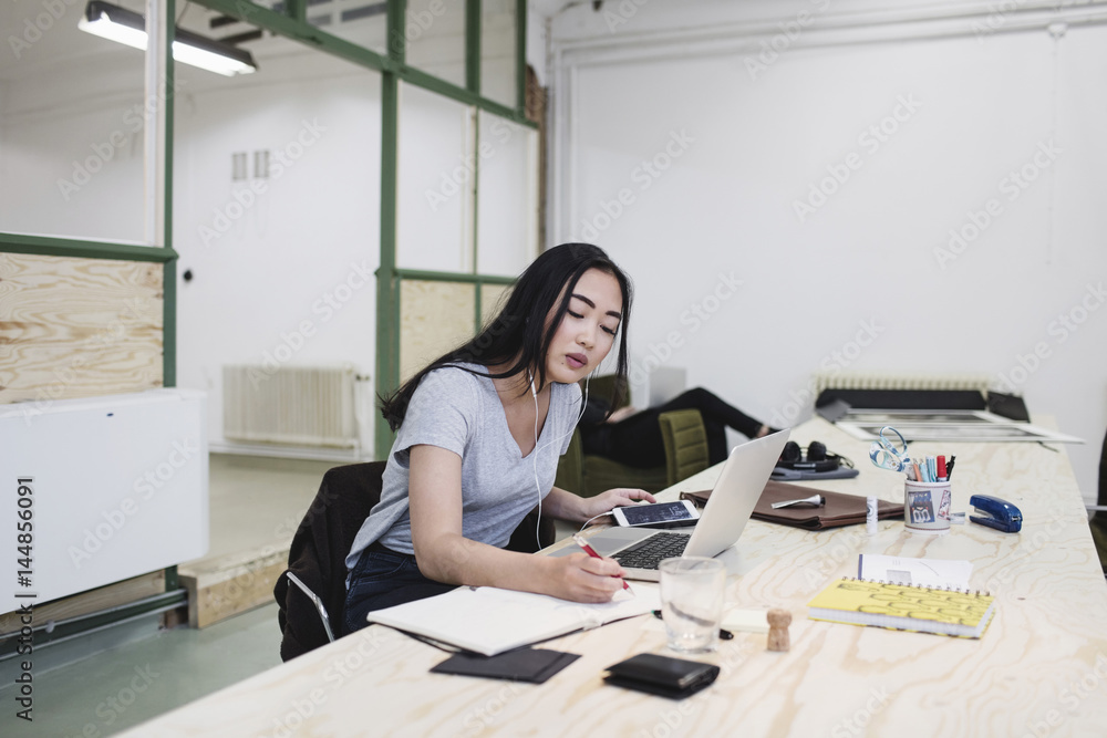 Young woman writing while working at desk in office Young woman writing while working at desk in office